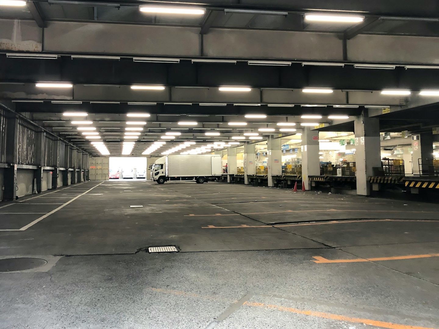 Camión de reparto blanco aparcado en el muelle de carga de un centro de distribución muy iluminado.